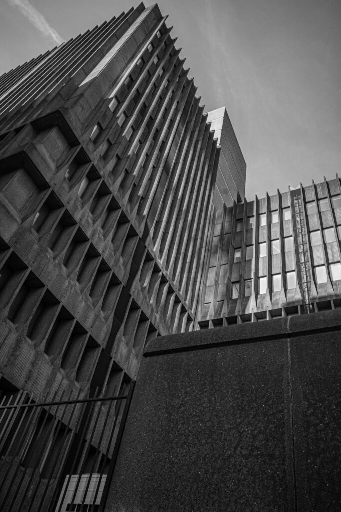 Low-angle black-and-white view of the brutalist Blakeburg building near Blaak, Rotterdam, showing its ribbed concrete facade and narrow windows against the sky.