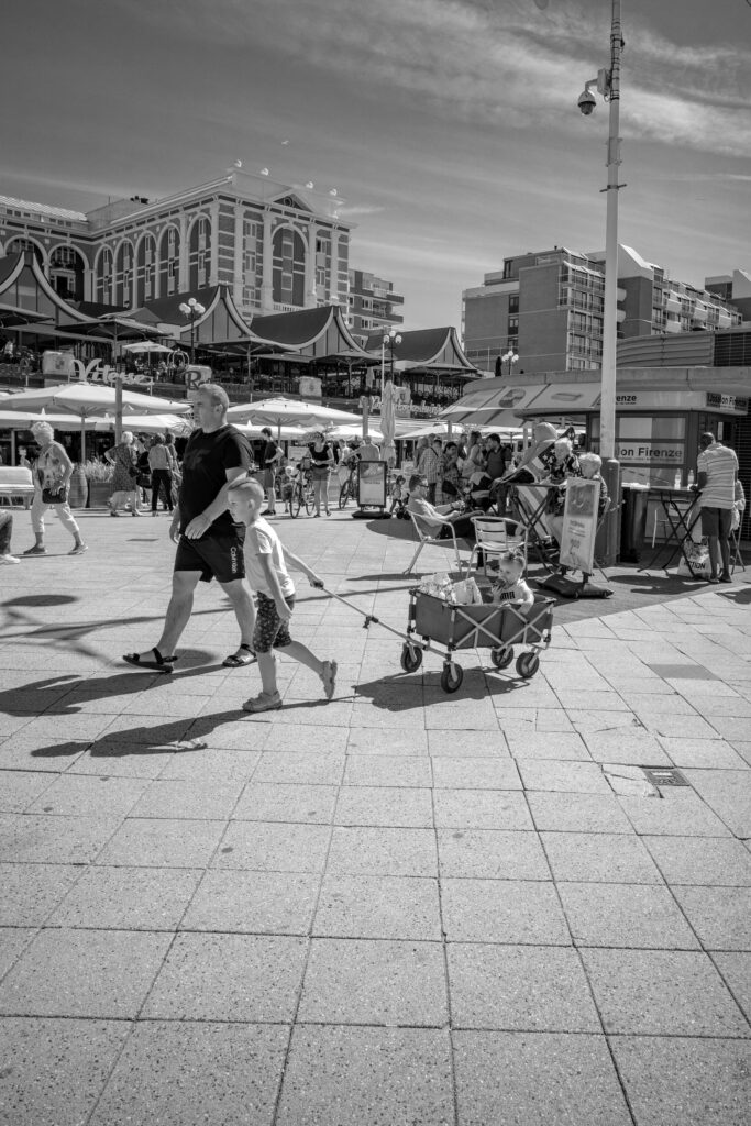 Child pulling handcart carrying brother along boulevard near Kurhaus Scheveningen