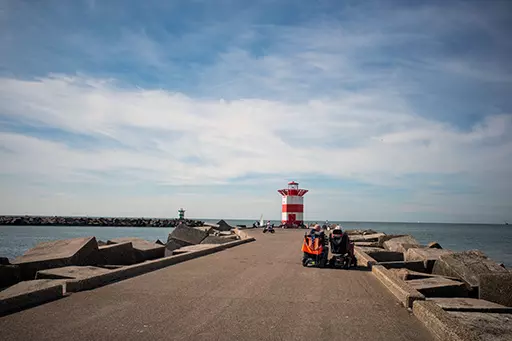 People resting on the northern harbor head of Scheveningen with the lighthouse at the end of the pier.